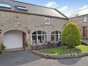 A stone building with a garage, two windows, and a small garden with a potted plant and a neatly trimmed bush.