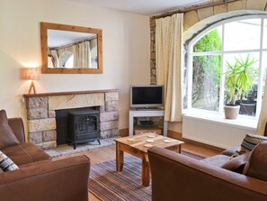 A living room with a stone fireplace, a television, and a large window with a view of greenery.
