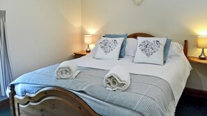 A neatly made bed with a blue and white striped bedspread, two pillows with floral embroidery, and two rolled towels. There is a wall decoration with the word "LOVE" and two bedside lamps. - 2 bedroom accommodation in Sewerby, near Bridlington (Sewerby, near Bridlington)