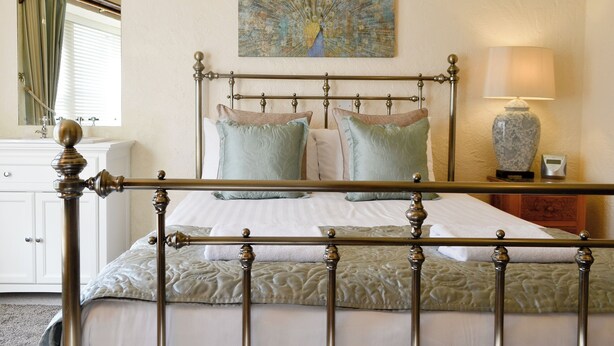 Un lit avec un cadre en métal, une lampe de chevet, un tableau au mur et une fenêtre avec des rideaux.
