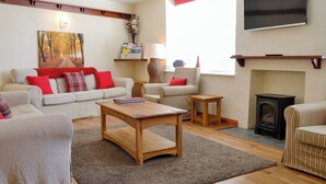 Un salon comprenant un canapé, des fauteuils, une table basse, une cheminée, un téléviseur et un tableau accroché au mur.