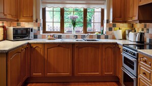 A kitchen with wooden cabinets, a microwave, a sink, and a window with a view of greenery.