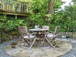 A wooden outdoor table with chairs, surrounded by a stone patio.