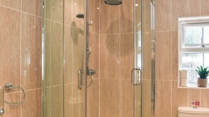Une douche fermée par des parois en verre, dotée d’un pommeau de douche à main et d’un robinet à main.