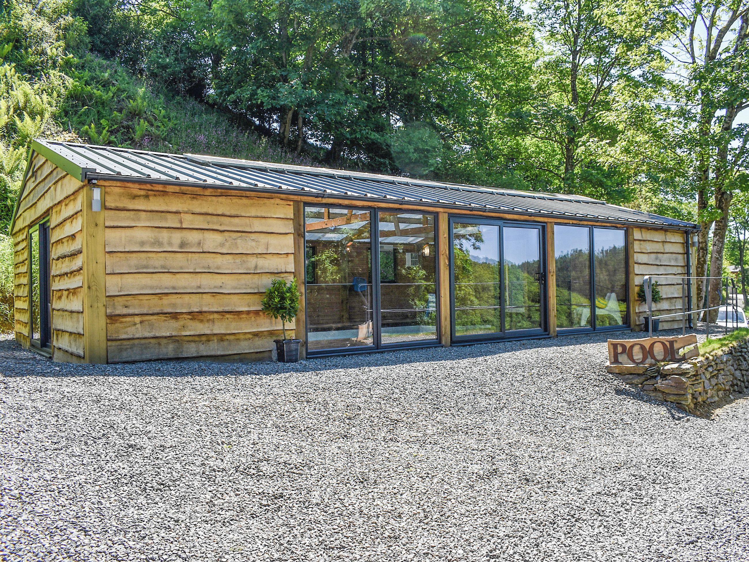 A wooden cabin with large sliding glass doors, a gravel driveway, and a sign indicating a pool.