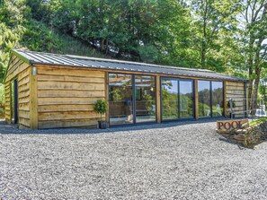 A wooden cabin with large sliding glass doors, a gravel driveway, and a sign indicating a pool.