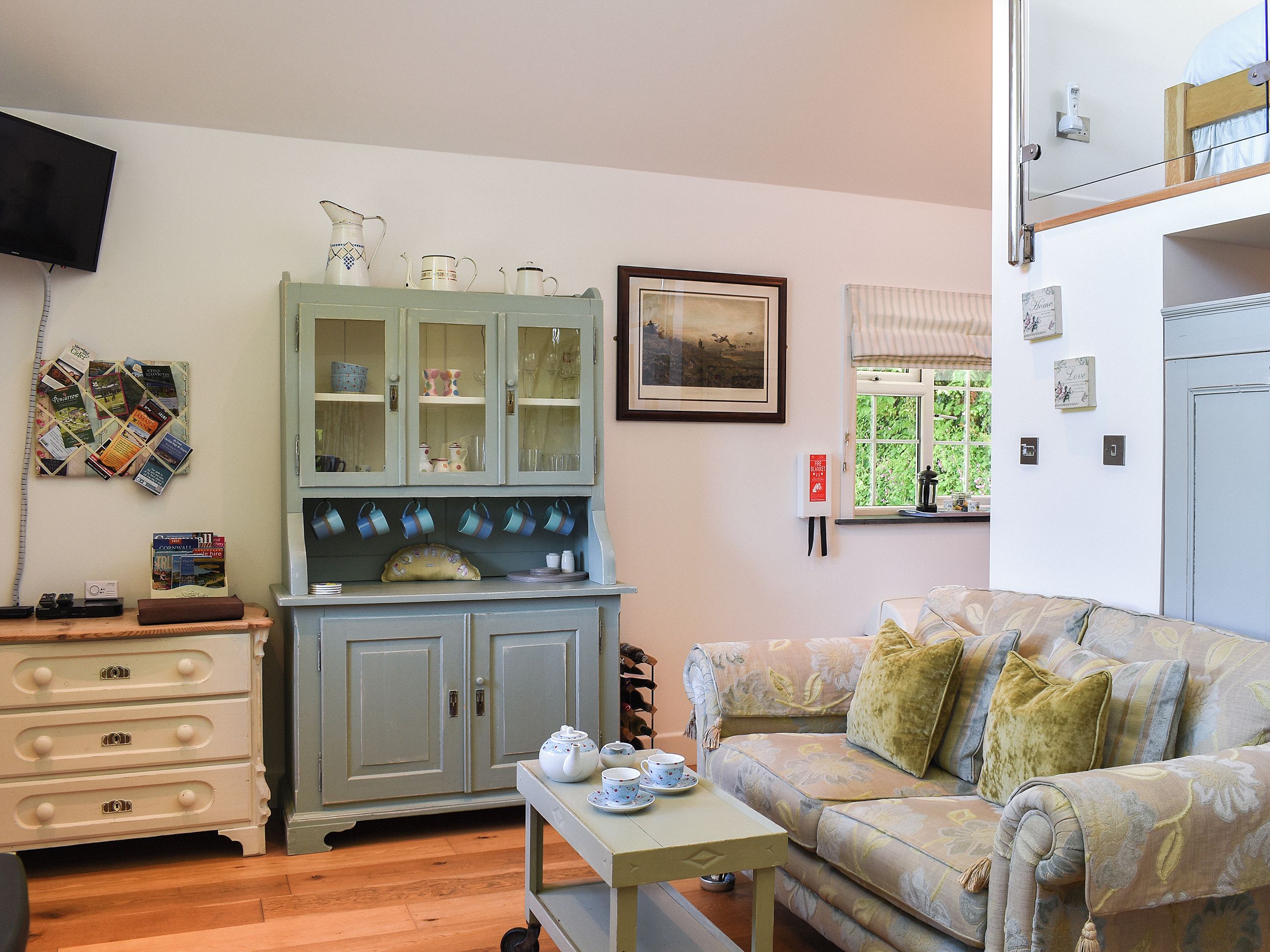 Una sala de estar con sofá, un mueble con puertas de vidrio, televisor y ventana con vista a follaje.