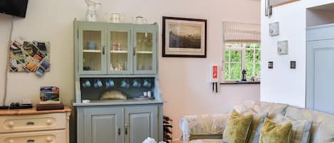 Una sala de estar con sofá, un mueble con puertas de vidrio, televisor y ventana con vista a follaje.