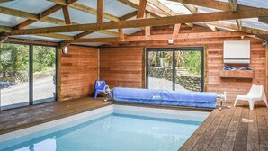 Ein Hallenbad mit Holzbalken, einer blauen Poolabdeckung und einem weißen Stuhl.