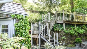 Eine Holztreppe führt zu einer Steinmauer, im Vordergrund befindet sich ein Garten.