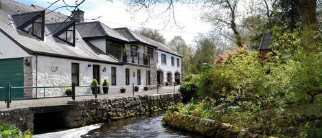 Un edificio blanco con un puente de piedra sobre un río, rodeado de follaje y árboles.