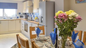 A modern kitchen with white cabinets, a refrigerator, and a dining area with a table set for two. - 3 bedroom accommodation in New Quay (New Quay)