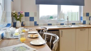 A kitchen with a breakfast setup including plates, a pitcher, and a vase of flowers. - 3 bedroom accommodation in New Quay (New Quay)