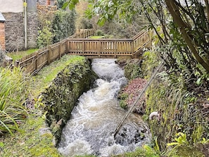 A wooden bridge over a flowing stream in a lush garden setting.