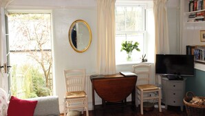 Una habitación acogedora con un escritorio de madera, dos sillas blancas, un televisor y una estantería.