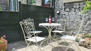 Un patio con una mesa redonda y cuatro sillas, una botella de vino y una maceta con flores.