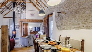 A cozy dining area with a wooden table set for breakfast, a stone wall, and a rustic interior.