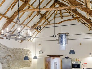 A rustic kitchen with exposed wooden beams, hanging pendant lights, and a stone wall. - The Threshing Barn - HSSW (Patchole, near Barnstaple)