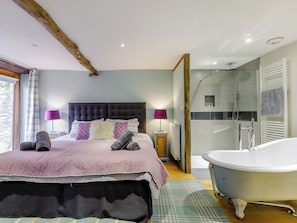 Une chambre avec un grand lit, une table de chevet et une lampe, ainsi qu’une salle de bain dotée d’une baignoire et d’une douche.