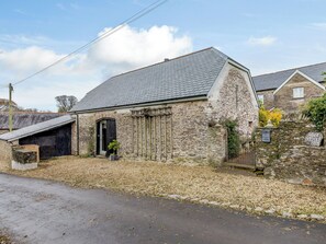 A stone building with a sloped roof, a small garden, and a paved road in front. - The Threshing Barn - HSSW (Patchole, near Barnstaple)