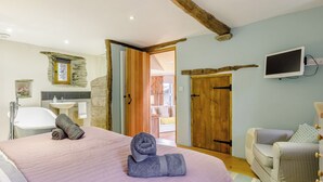 A bedroom with a large bed, a wooden door, a television, and a bathroom with a bathtub and sink.