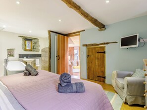A bedroom with a large bed, a wooden door, a television, and a bathroom with a bathtub and sink. - The Threshing Barn - HSSW (Patchole, near Barnstaple)