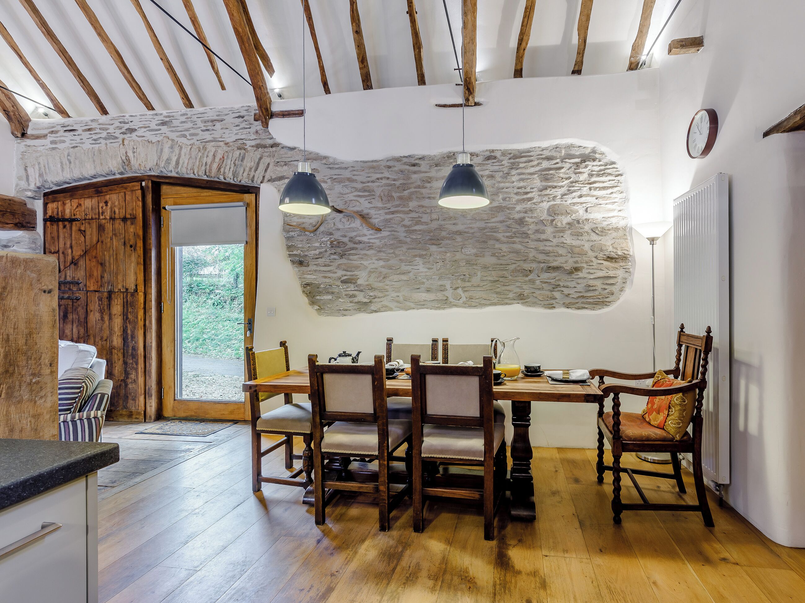 A rustic dining area with a stone wall, wooden ceiling beams, and a wooden table set for two.