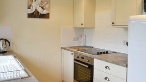 Eine kompakte Küche mit weißen Schränken, einem eingebauten Backofen, einem Wasserkocher und einem Blumenbild an der Wand.