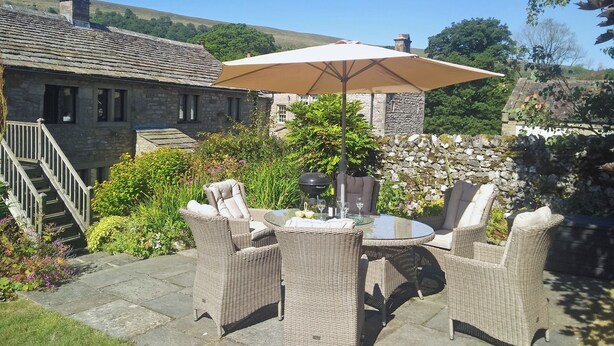 A patio with wicker furniture and a table, surrounded by stone walls and greenery. - 3 bedroom accommodation in Starbotton, near Skipton (Starbotton, near Skipton)