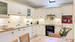 A modern kitchen with white cabinets, a wooden dining table, and a red microwave. - 3 bedroom accommodation in Starbotton, near Skipton (Starbotton, near Skipton)