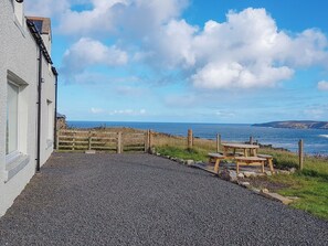 A gravel pathway leading to a wooden table and chairs by a white building with a view of the sea. - 3 bedroom accommodation in Armadale, near Bettyhill (Armadale, near Bettyhill)