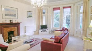 A living room with a fireplace, a sofa, a television, and large windows. - 3 bedroom accommodation in Ventnor (Ventnor)