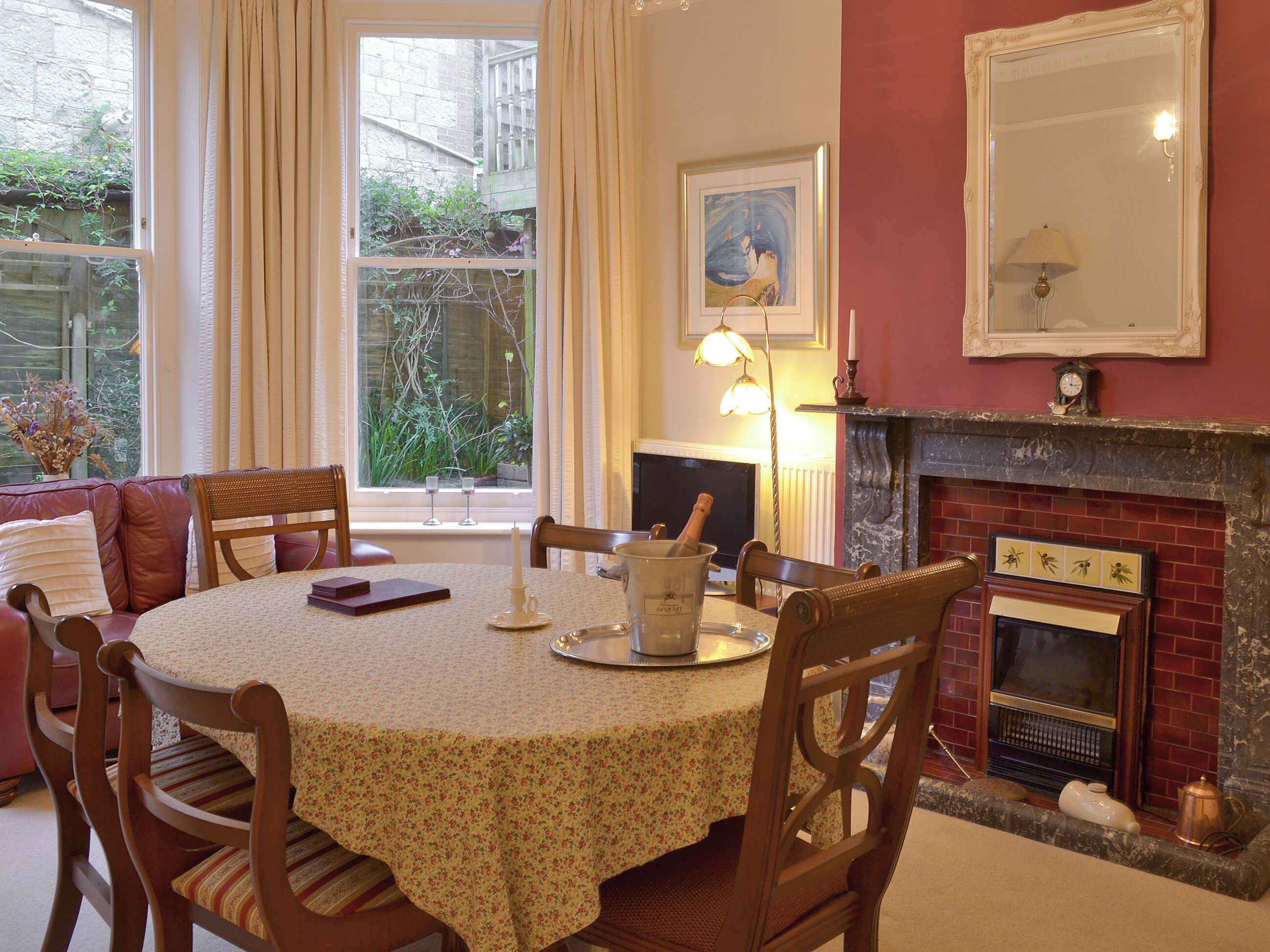 A dining room with a table set for four, a fireplace, and a window with curtains.