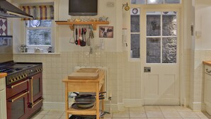 A kitchen with a stove, oven, wooden shelf with kitchen utensils, a television, and a window with curtains. - 3 bedroom accommodation in Ventnor (Ventnor)