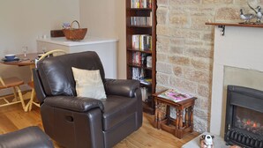 A living room with a leather sofa, a bookshelf, a fireplace, and a small table with decorative items. - 1 bedroom accommodation in Curbar, near Bakewell (Curbar, near Bakewell)