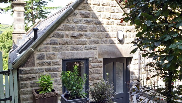 A stone cottage with a steeply pitched roof, a chimney, and a door with glass panels. There are three potted plants in front of the cottage. - 1 bedroom accommodation in Curbar, near Bakewell (Curbar, near Bakewell)