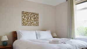 A neatly made bed with white linens and a folded towel, a bedside table with a lamp, and a wall art piece above the bed. - 4 bedroom accommodation in St Monans, near Anstruther (St Monans, near Anstruther)