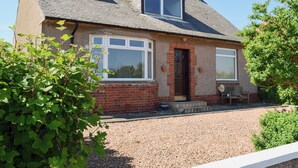 A two-story house with a brick facade, a small porch with a bench, and a gravel driveway. - 4 bedroom accommodation in St Monans, near Anstruther (St Monans, near Anstruther)