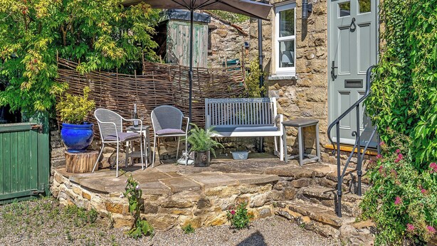 Ein Steinhaus mit einer Terrasse, die eine Bank, Stühle und einen Tisch bietet.