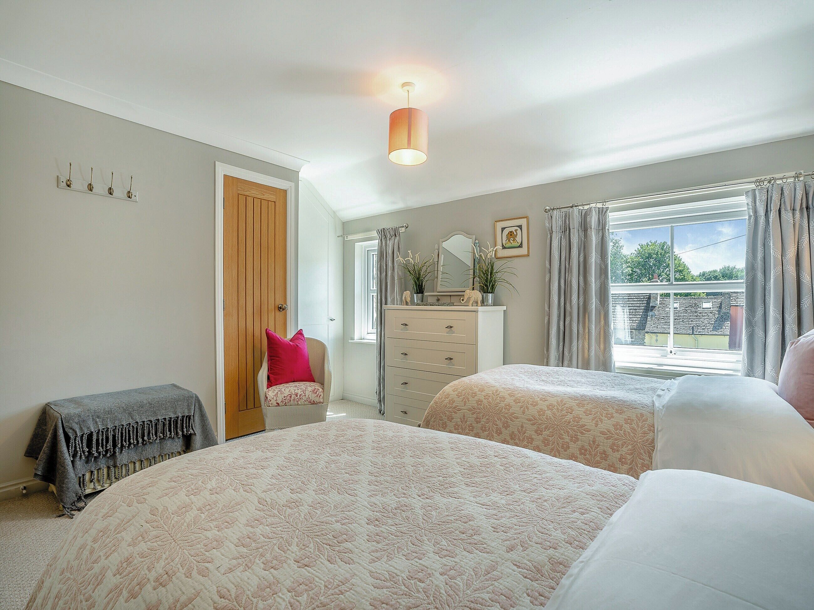 A bedroom with two beds, a dresser, a mirror, and a window with curtains.