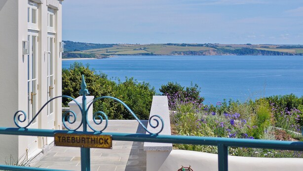 A view of the sea from a balcony with a 'TREBURTHICK' sign, a white building, and a metal railing. - 8 bedroom accommodation in Porthpean, near Charlestown (Porthpean, near Charlestown)