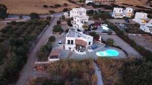 Una villa blanca con piscina, rodeada de vegetación y otras construcciones blancas.