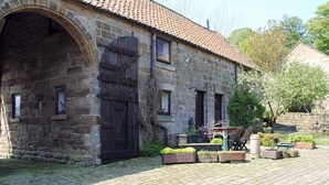 A stone building with a tiled roof, a large arched doorway, and a small porch with potted plants. - THRESHING BARN - KZA (Glaisdale, near Whitby)
