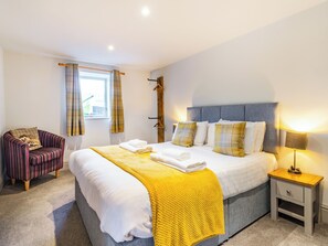 Une chambre bien rangée, avec un lit, une chaise, une table de chevet et une fenêtre avec des rideaux.