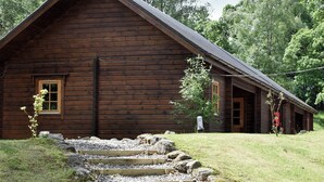 A rustic log cabin with a steep gabled roof, surrounded by a grassy area and trees. - 2 bedroom accommodation in Killin, near Crianlarich (Killin, near Crianlarich)