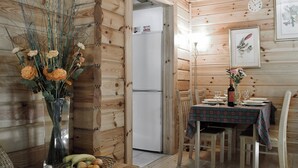 A wooden cabin interior with a dining table set for two, a refrigerator, and a vase with flowers. - 2 bedroom accommodation in Killin, near Crianlarich (Killin, near Crianlarich)