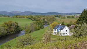 A white house with a blue roof, surrounded by green fields and a river.
