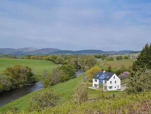 Une maison blanche avec un toit bleu, entourée de champs verdoyants et d’une rivière.