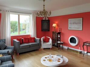 A living room with a grey sofa, a white armchair, a round coffee table, a chandelier, and a fireplace.