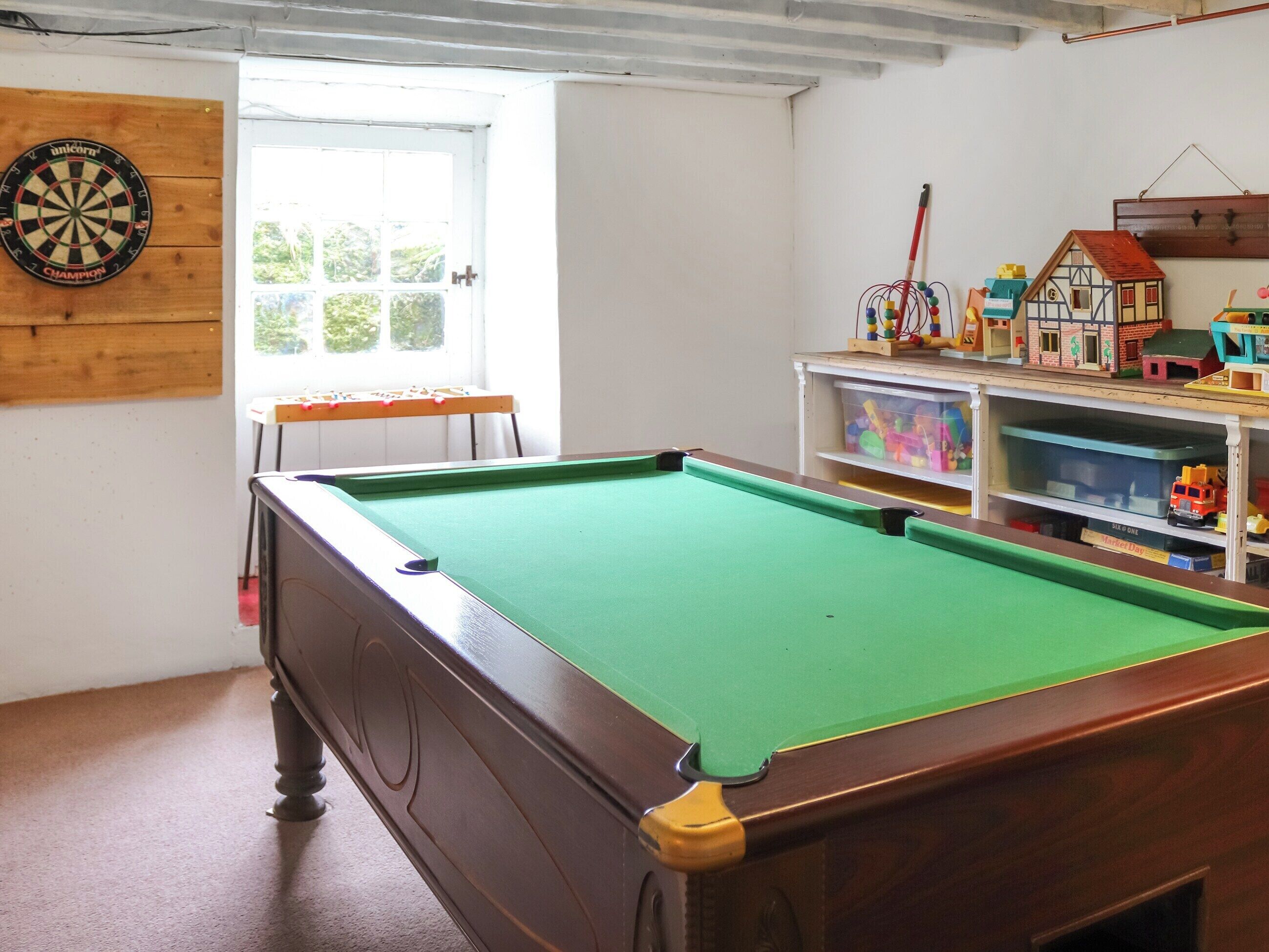 A pool table in a room with a dartboard, a window, and a toy house display.